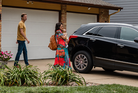 A photo of a woman walking to a vehicle while holding a baby and a man walking behind her